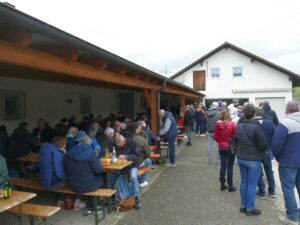 Menschen sitzen unter einer Pergola an Bierbänken und essen.