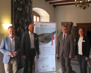 Vier Personen vor einem Informationsbanner des Naturparks Neckartal-Odenwald bei der Mitgliederversammlung in Mosbach.
