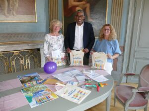 Drei Personen präsentieren im Rathaus das Nachbarschafts-Fest-Starter-Set mit Infomaterial, Luftballons und Stofftaschen.