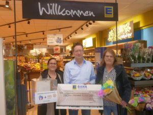 Drei Personen mit einem großen Spendenscheck und einer Spendenbox vor dem Eingang von Edeka Walter.
