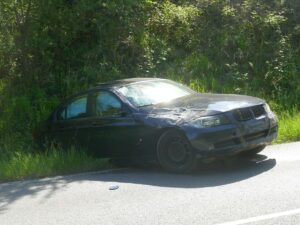 Stark beschädigter BMW im hohen Gras neben der Straße nach Unfall