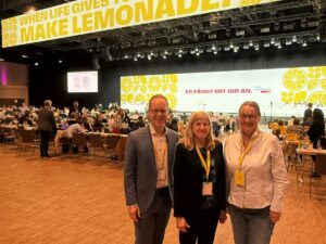 Jens Brandenburg, Claudia Felden und Ulrike von Eicke stehen vor der Bühne beim FDP-Bundesparteitag 2025 in Berlin.