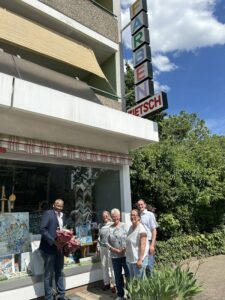 Fünf Personen stehen lachend vor einem Schaufenster mit Kunstwerken bei Farben Zietsch in Leimen; OB Ehret hält einen Blumenstrauß.