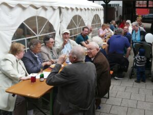 Besucher sitzen an langen Tischen im Freien bei der AWO-Vatertagsfeier.