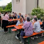 Menschen an Bierzeltgarnituren beim Fest neben der Kirche.