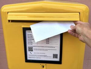 Nahaufnahme eines gelben Briefkastens der Deutschen Post mit einem Einwurf eines Briefes.