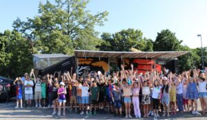 Gruppenfoto von Schulkindern vor dem SolarButterfly mit ausgebreiteten Solarpaneelen, die Kinder heben fröhlich die Arme.