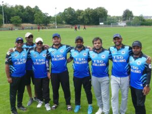 Acht Cricket-Spieler in blauen TSG-Stallions-Trikots Arm in Arm auf dem Rasen.