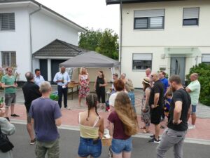 Menschen stehen auf einer neu asphaltierten Straße in einem Wohngebiet, im Rahmen eines Nachbarschaftsfests.