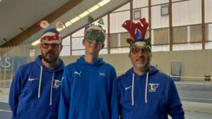 Drei Trainer in blauen Hoodies mit lustigen Weihnachtsbrillen in der Tennishalle